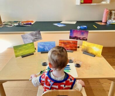 Young child painting at a table, surrounded by vibrant nature scenes, exploring creative expression through art.