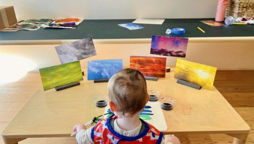 Young child painting at a table, surrounded by vibrant nature scenes, exploring creative expression through art.