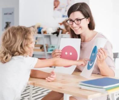 a child pointing to a happy smiley face on a sheet of paper held by a woman