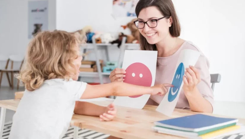 a child pointing to a happy smiley face on a sheet of paper held by a woman