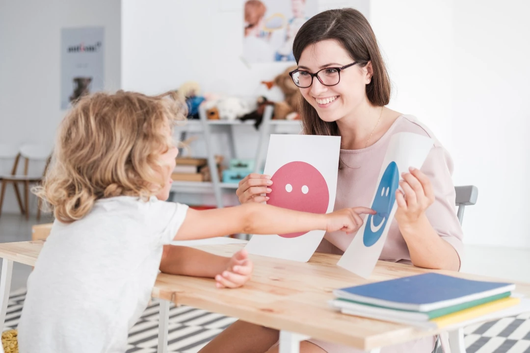 a child pointing to a happy smiley face on a sheet of paper held by a woman