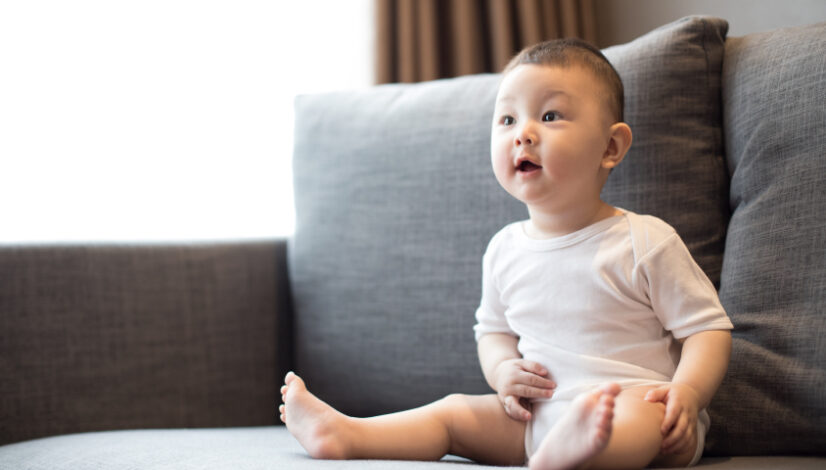 Infant sitting on a sofa showing early developmental behaviors and expressions, a topic covered in recognizing the early signs of autism in infants