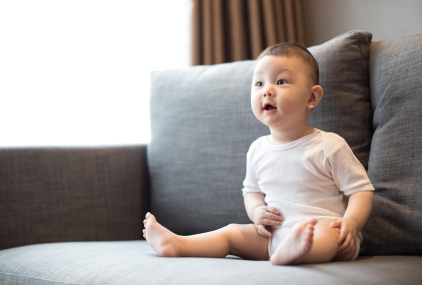 Infant sitting on a sofa showing early developmental behaviors and expressions, a topic covered in recognizing the early signs of autism in infants